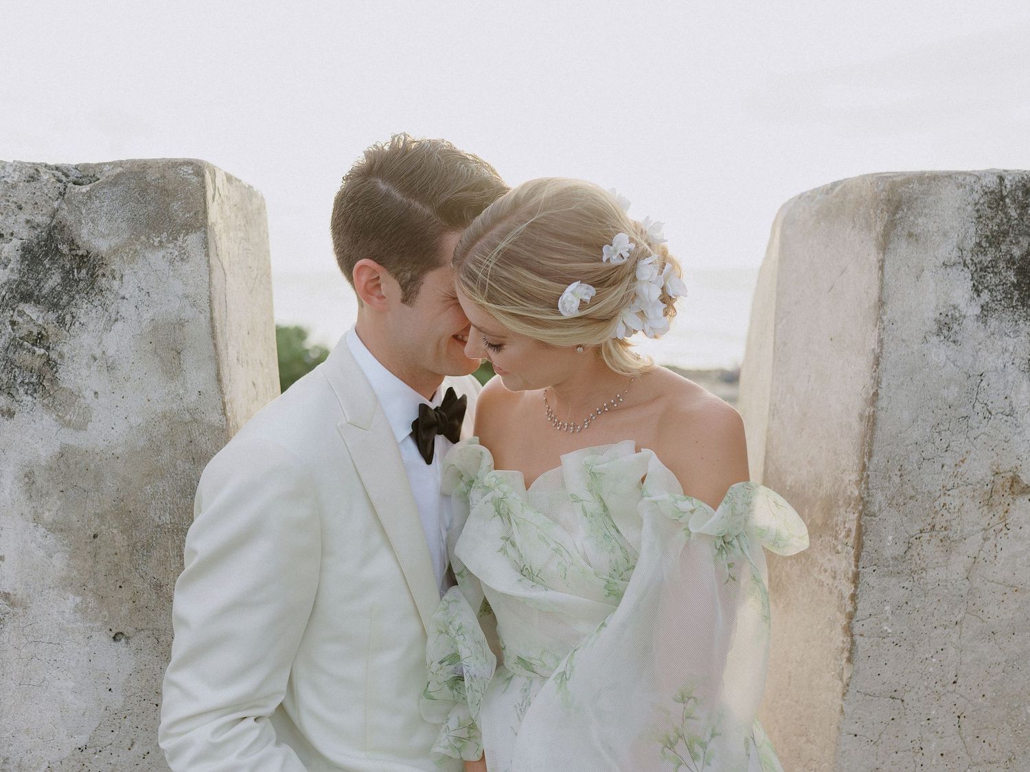 Romantic wedding couple in white embracing against stone wall.
