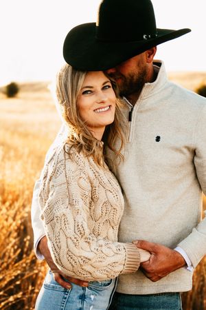 A romantic couple embraces in a golden wheat field at sunset wearing casual sweaters and denim.