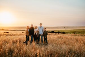 A family stands together in a golden wheat field at sunset on their ranch.