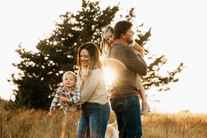 A couple dances together in a golden field at sunset while their child plays nearby.