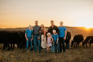 A ranch family poses together at sunset with their cattle grazing in the background.