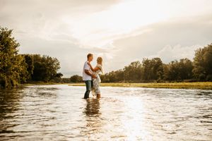 Couple standing in shallow water at sunset embracing and dancing together in a romantic lakeside moment.