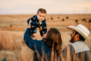 Family enjoying tender moments together in a golden wheat field at sunset.