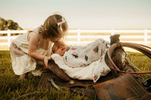 A leather saddle rests in a grassy field near a white fence during golden hour lighting.