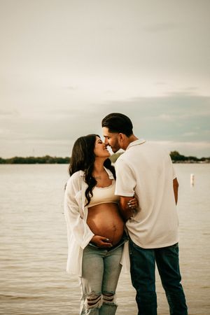 A couple shares an intimate moment together on a beach with a lake and cloudy sky in the background.