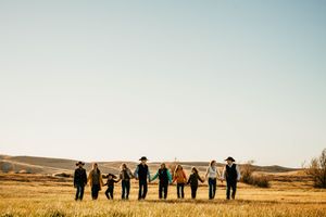 A group of people in black attire stand in silhouette against a golden field at sunset.