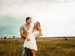 Couple sharing a romantic moment together in a golden field at sunset with round hay bales in the background.
