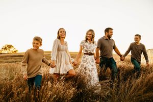 Family sits together in a golden field at sunset, creating a warm silhouette against the glowing sky.