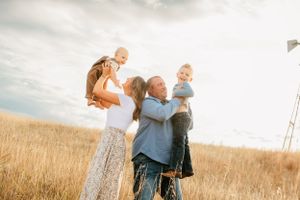 Family members embrace while standing in a sunlit field of tall grass.