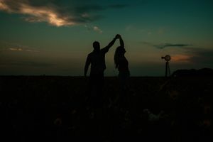 Silhouettes of people walking along a hilltop against a dramatic orange and teal sunset sky.