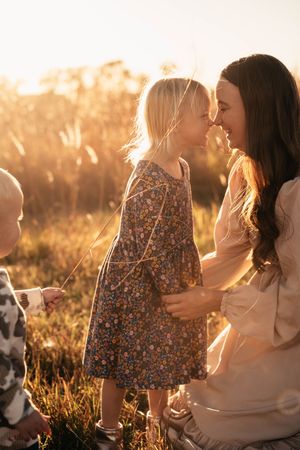 Mother and daughter share tender moments in a sunlit field with golden light streaming through their hair at sunset.