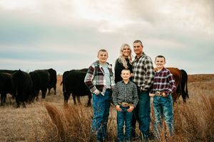 A family wearing casual denim and plaid clothing poses together in a golden autumn field at sunset.
