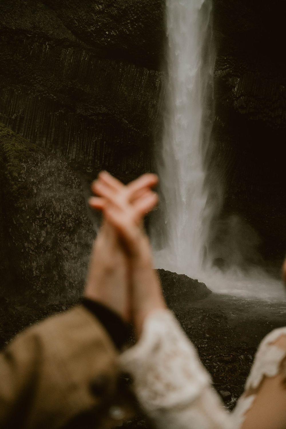Couple holds hands in front of a misty waterfall during their outdoor elopement.