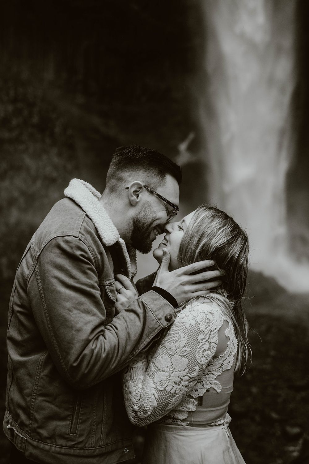 Black and white photo of couple nearly kissing in front of a dramatic waterfall.