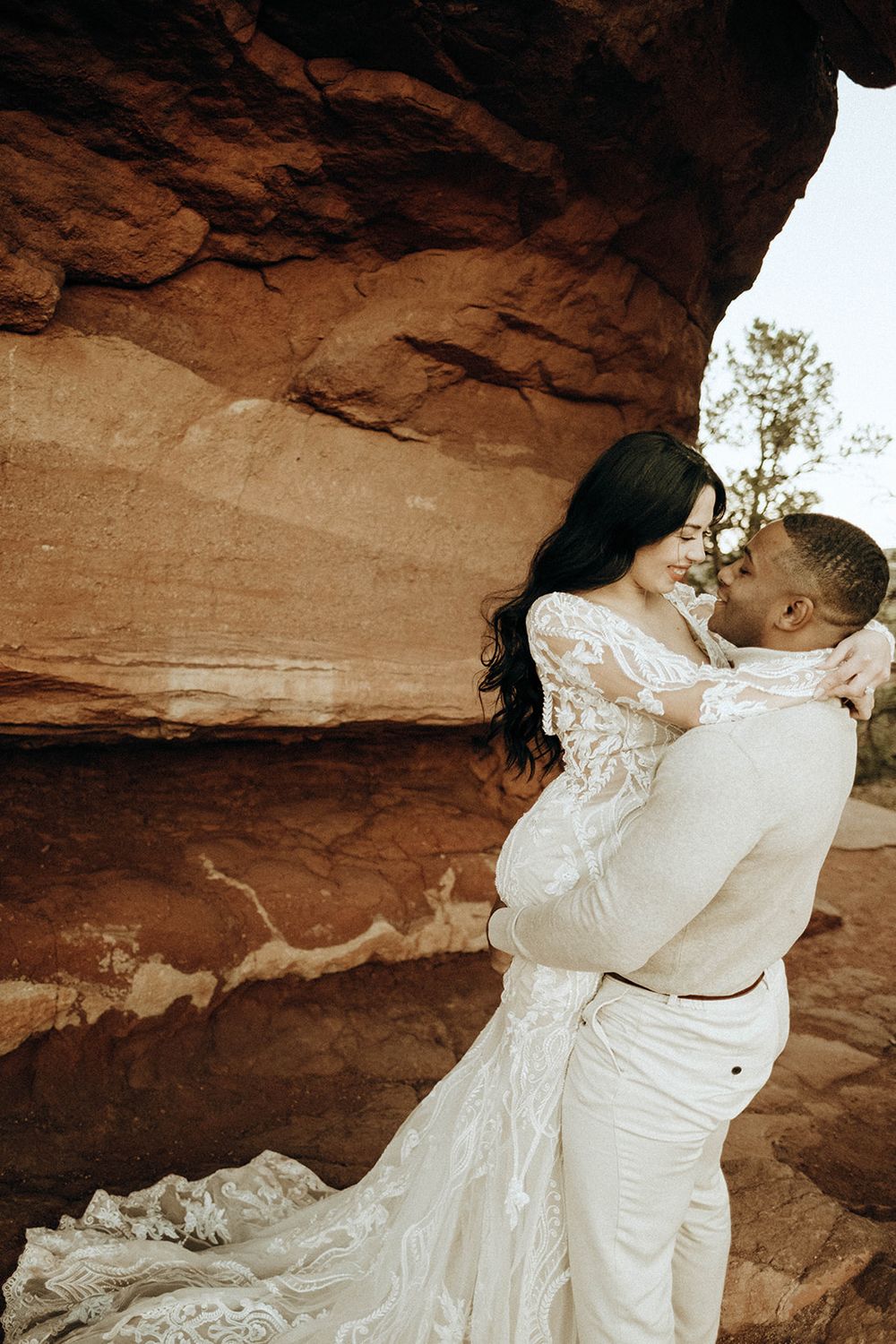 Bride and groom embrace tenderly against red sandstone rock formations at outdoor wedding.