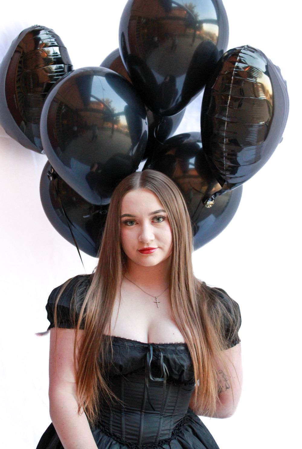 A gothic-styled photoshoot with black balloons and a person in a black corset dress against a white background.