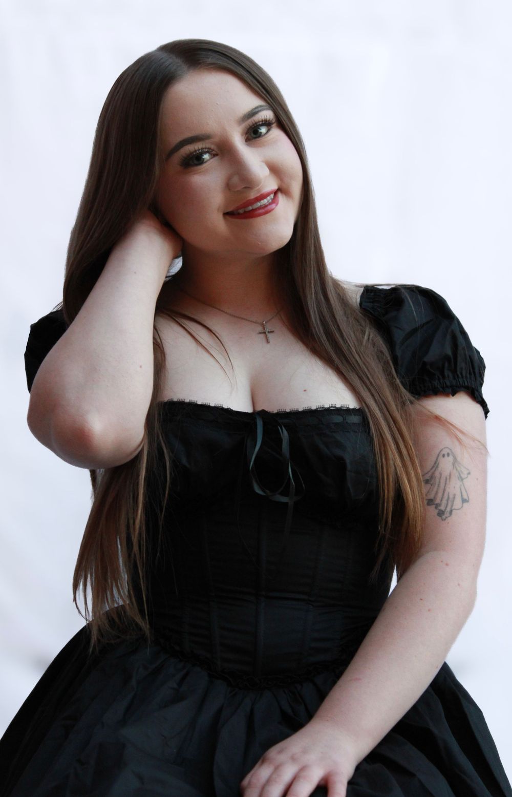 A portrait photo featuring someone wearing a black corset dress with puffy sleeves against a white backdrop.