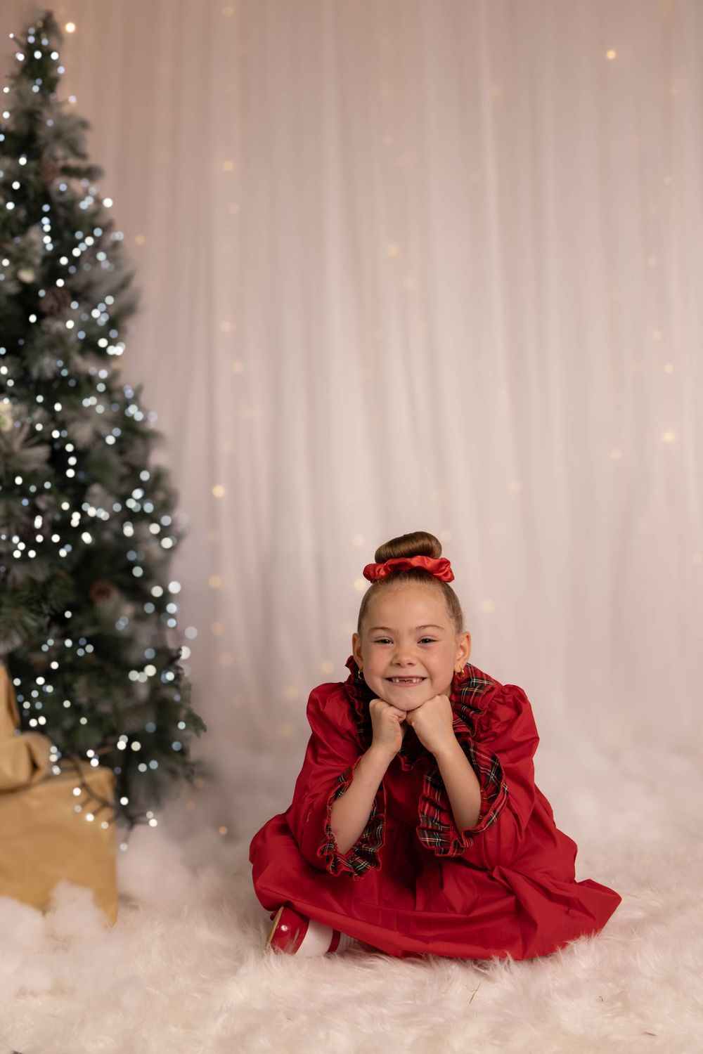 A festive Christmas portrait with a red dress against a backdrop of a decorated tree and white lights.