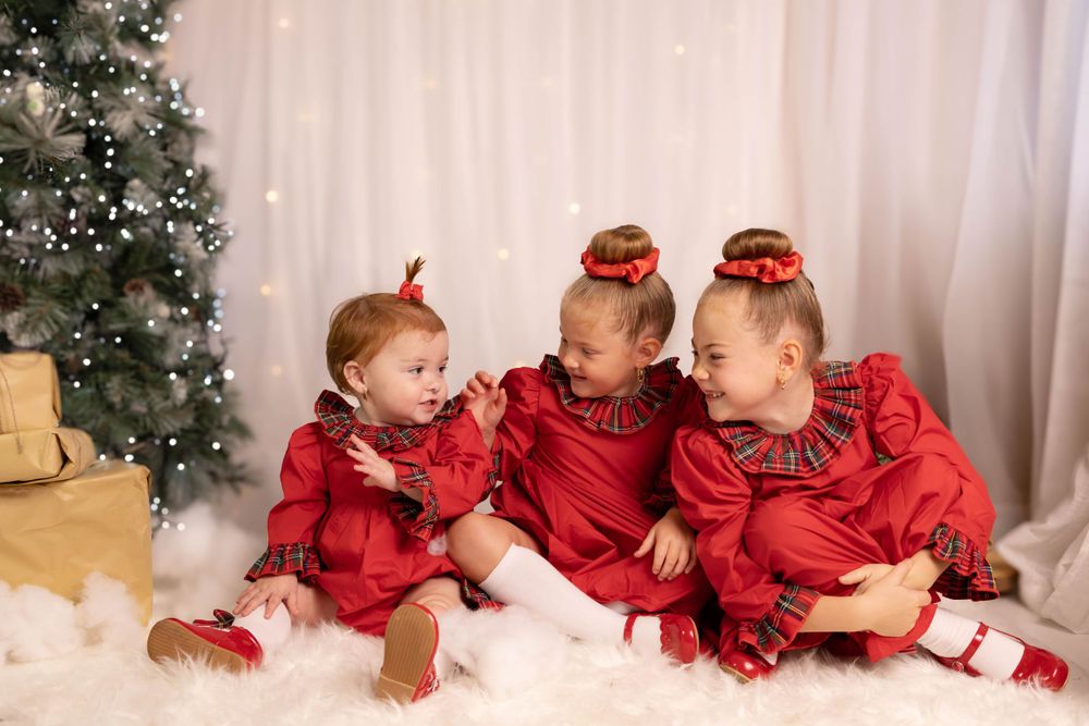 Holiday portrait of three children in matching red outfits sitting on white floor.