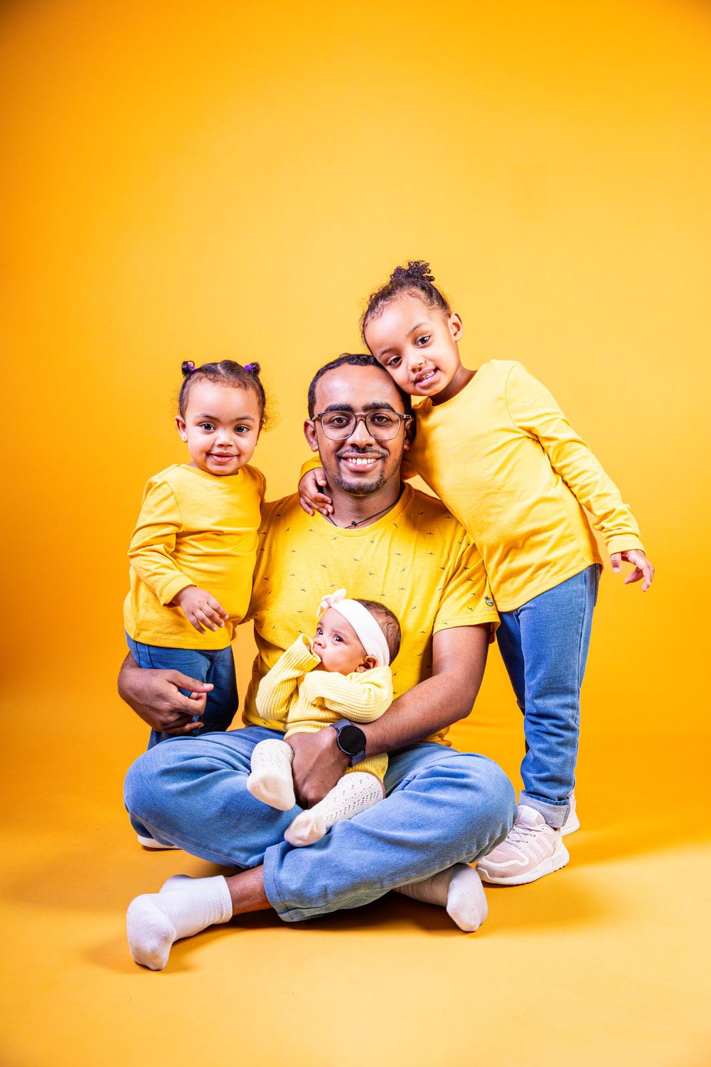 A family wearing matching yellow shirts poses together against a bright orange background.