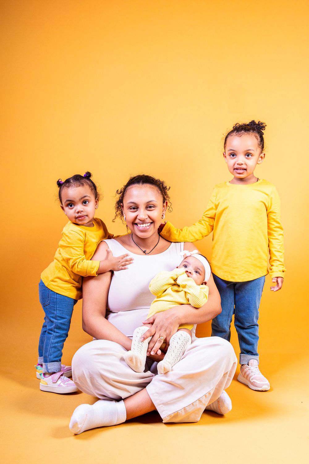A family group in coordinated yellow outfits sits together on an orange backdrop.