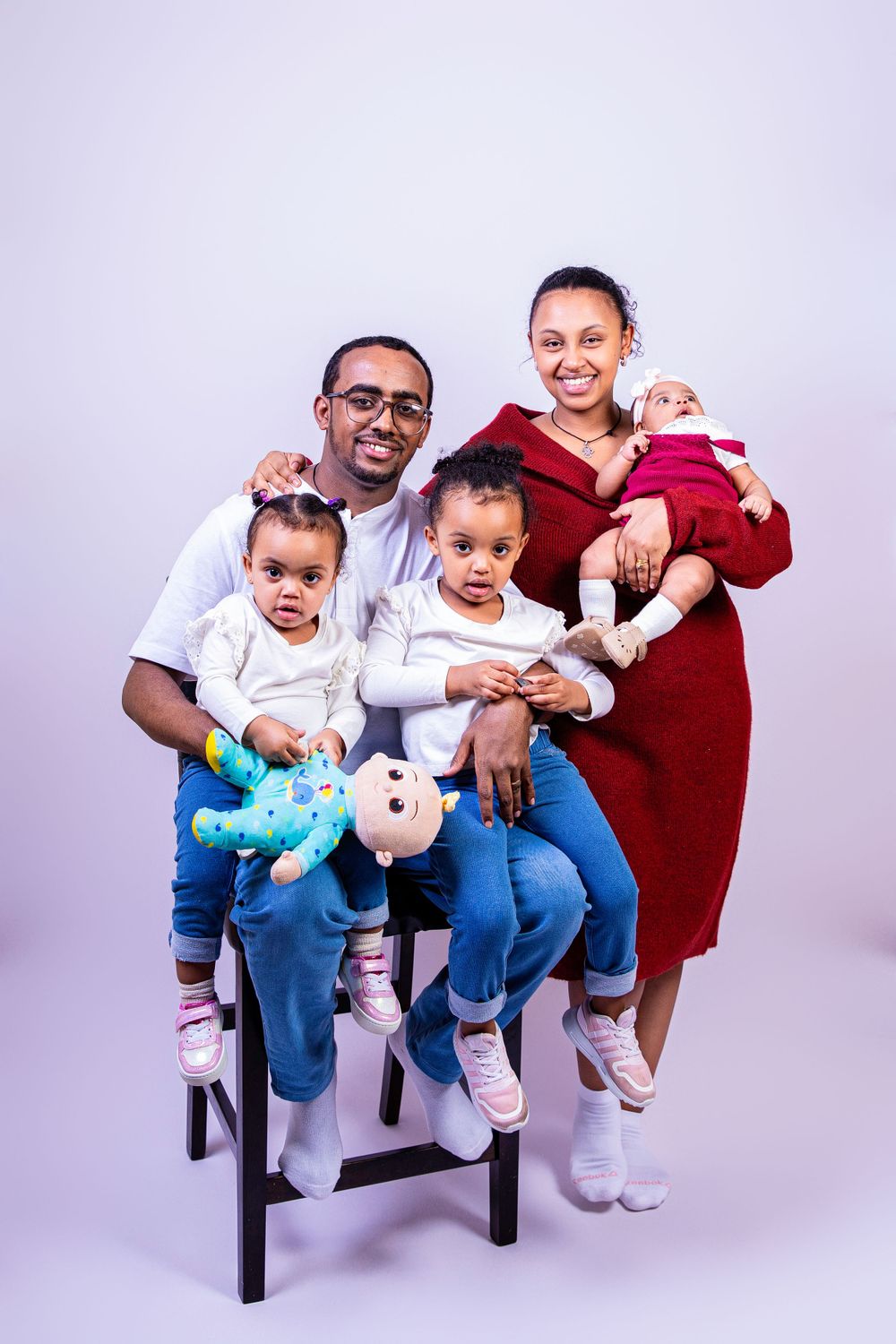 A studio family portrait with everyone wearing coordinating outfits against a light purple background.