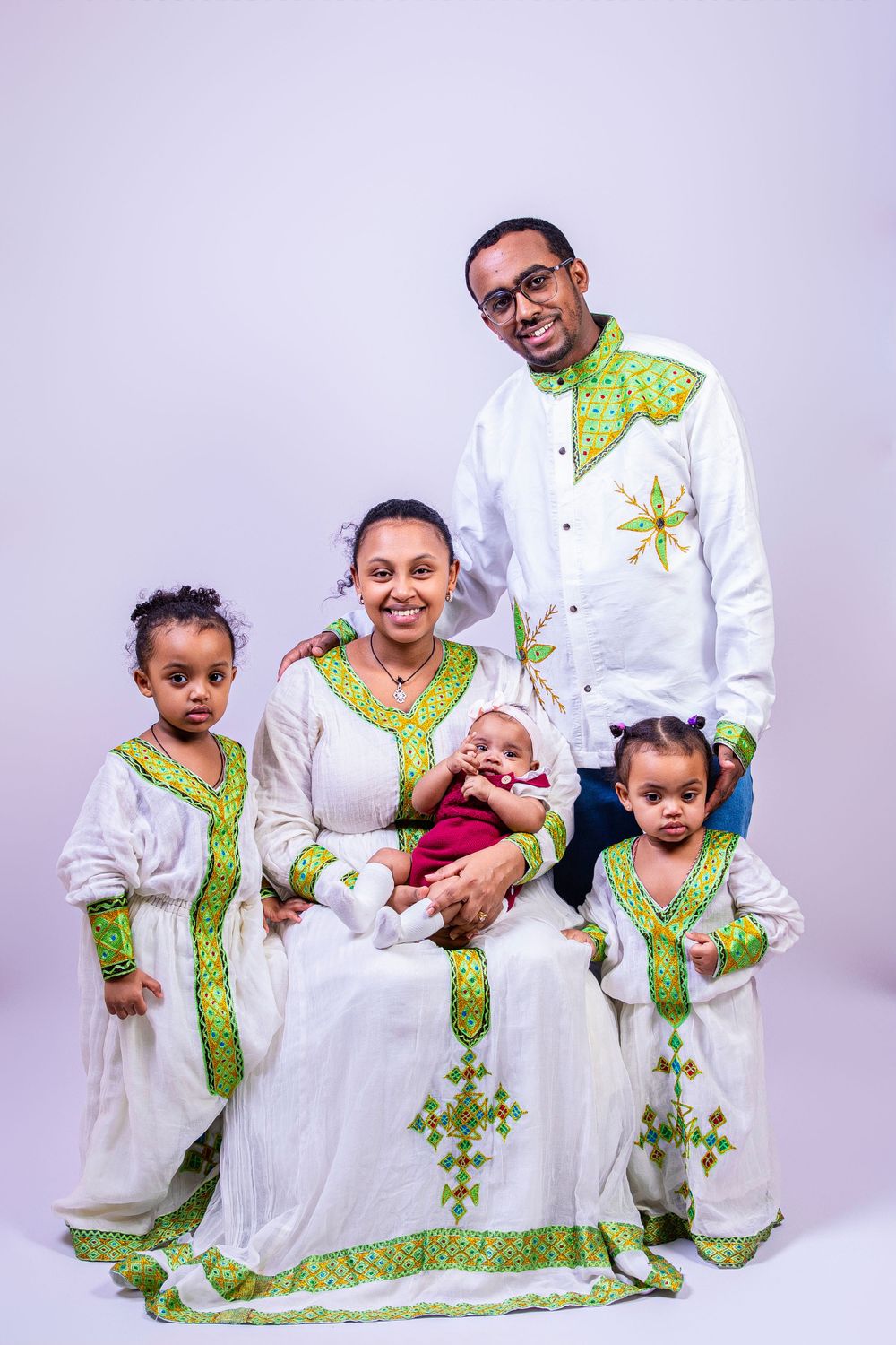 Family wearing coordinated traditional Ethiopian attire with white fabric and green accents.