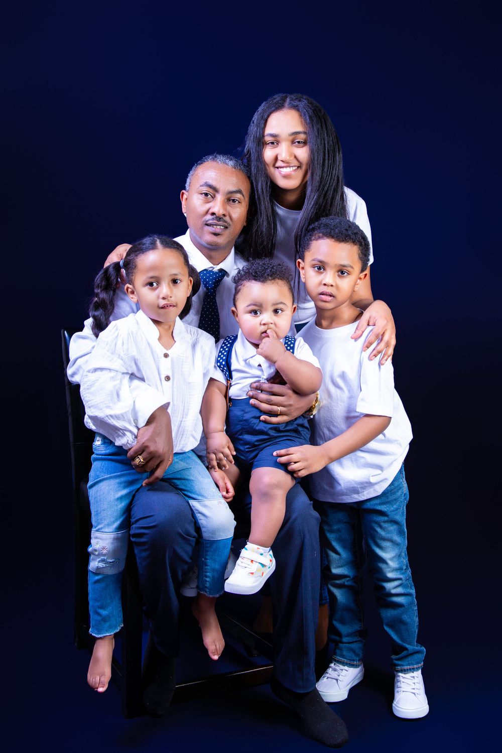 A family portrait against a dark blue background showing five people in coordinated outfits.