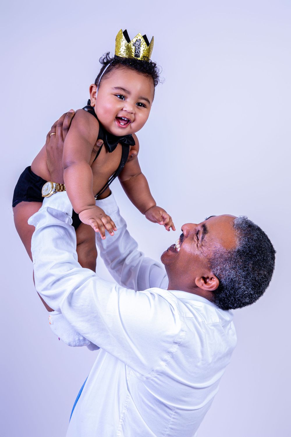 A playful moment captured as an adult lifts a child wearing a crown.