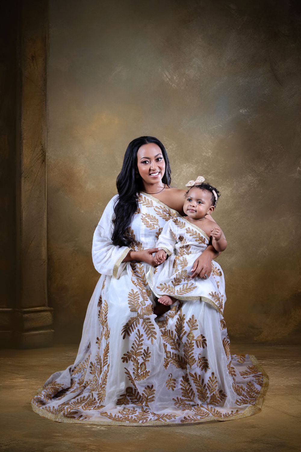 Studio portrait featuring matching white and gold dresses in formal setting.