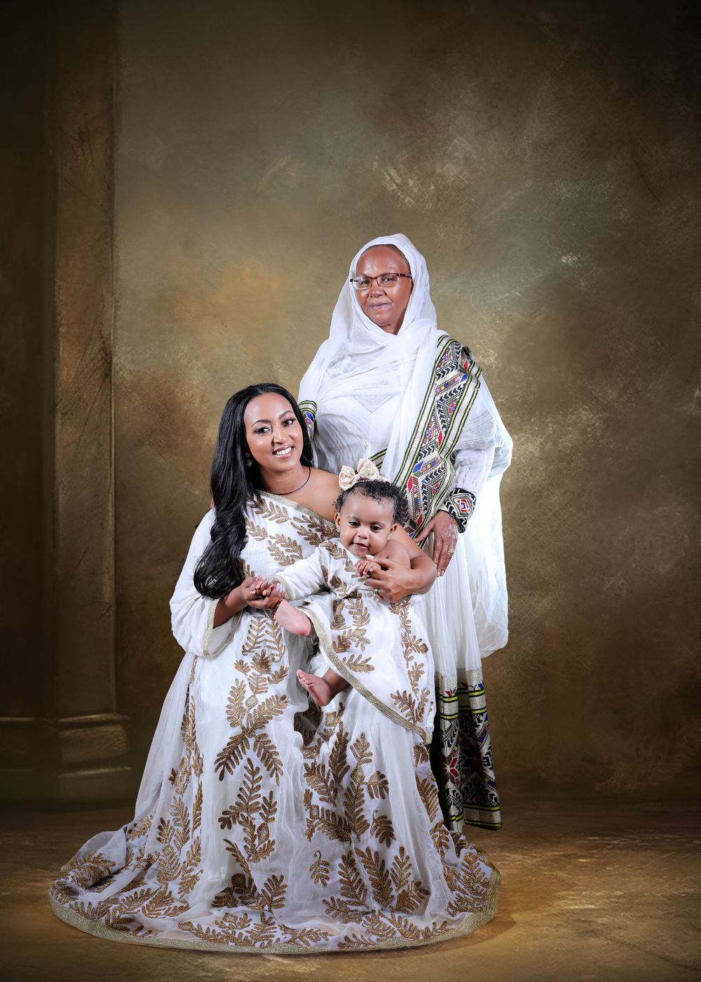 Three generations pose in coordinating white and gold formal attire for studio portrait.