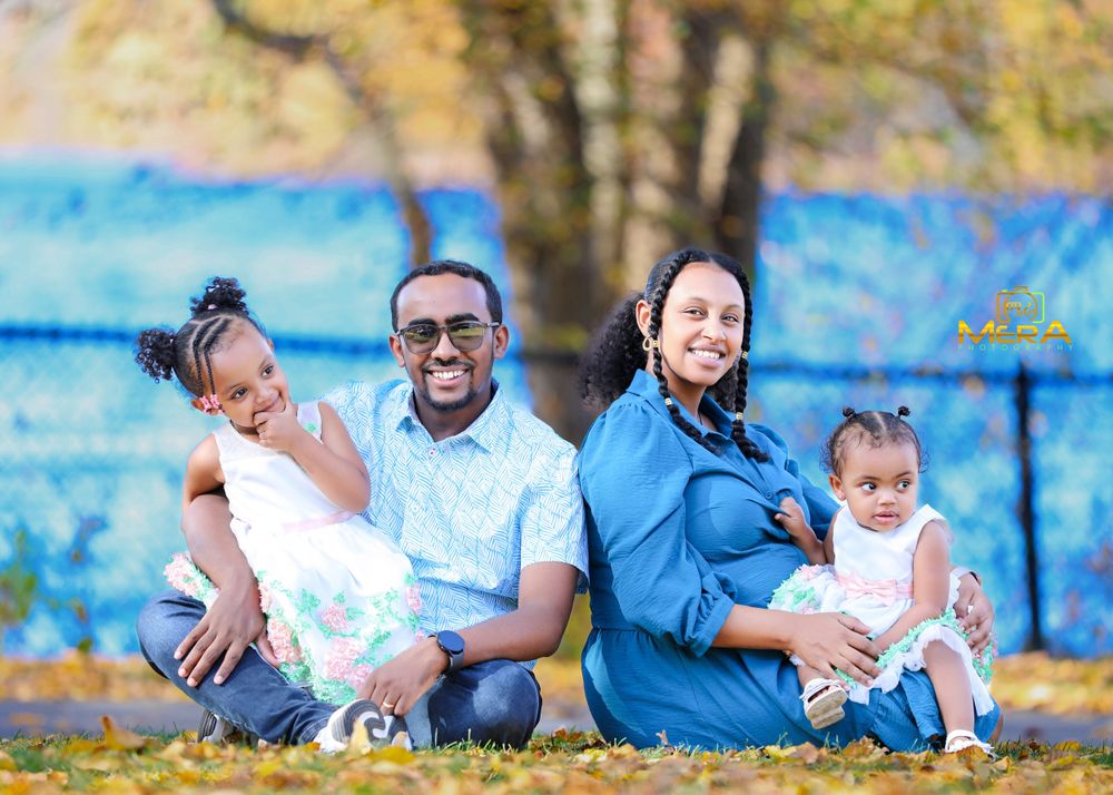 A family sits together on autumn grass with a blue backdrop during an outdoor photoshoot.