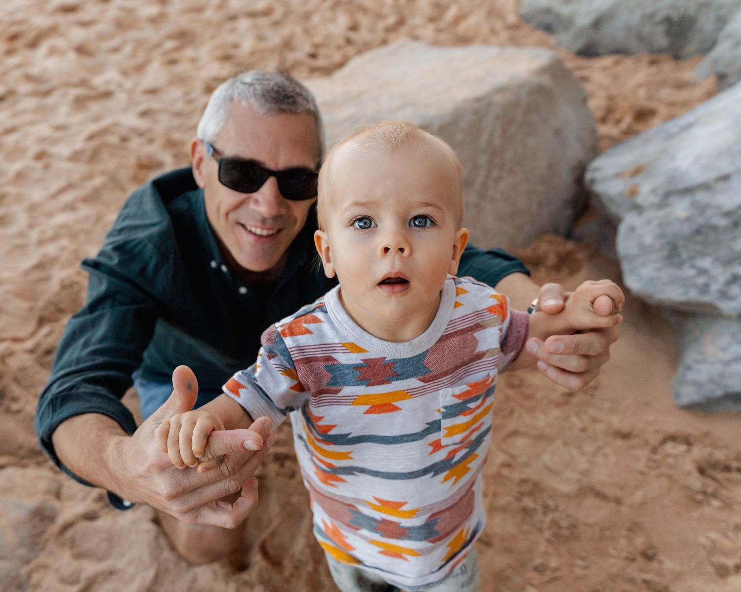 toddler-boy-and-his-dad-looking-into-the-camera-among-the-rokcs-at-a-family-photoshoot