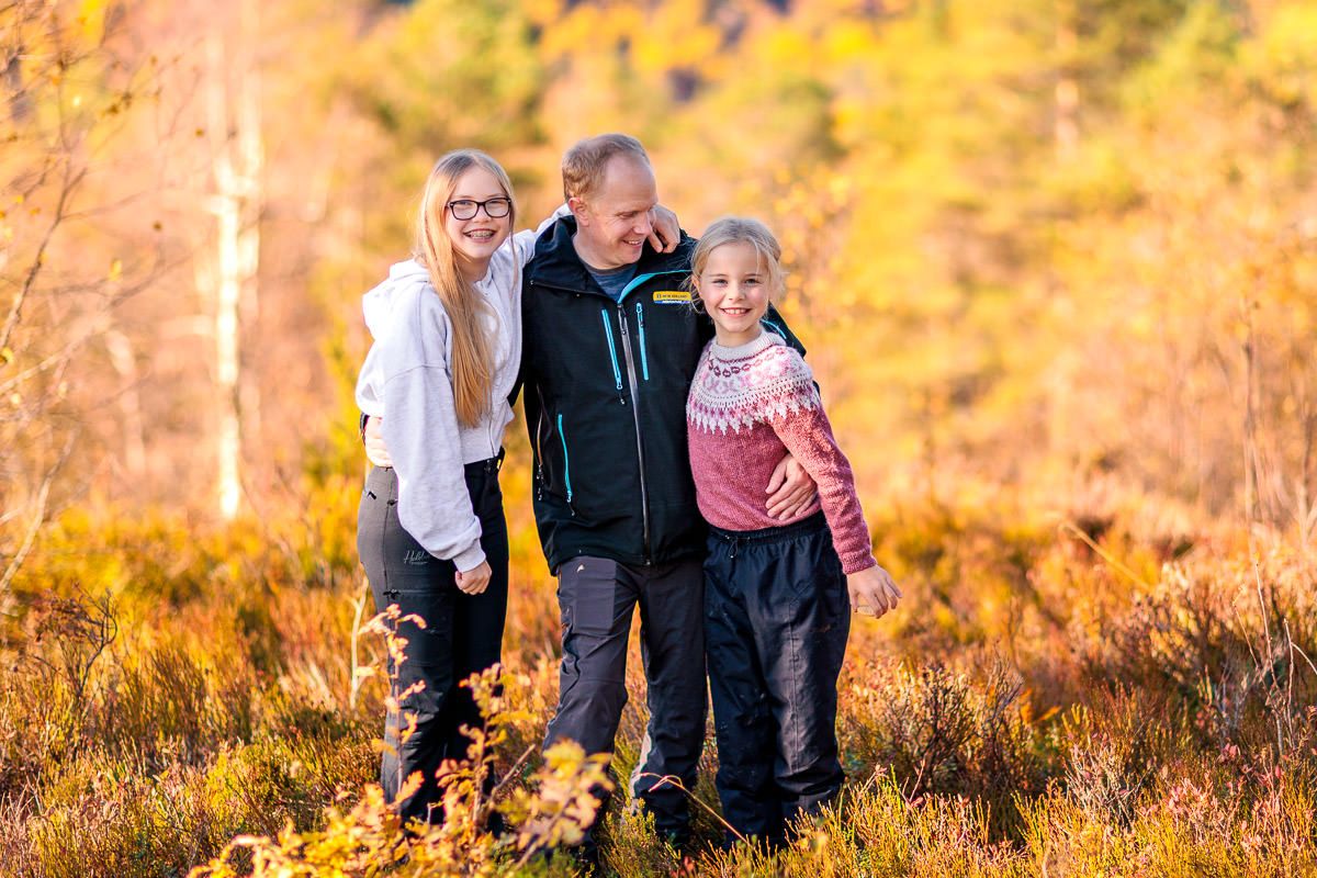 Far og to døtre står sammen i en solfylt skog på Naglestad i høstfarger.