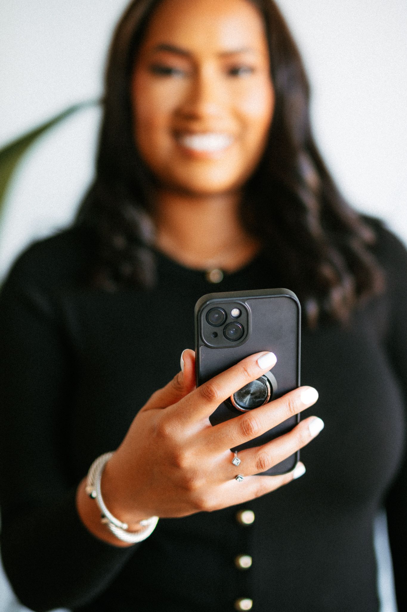 Person in black sweater holding iPhone with PopSocket and wearing silver jewelry.