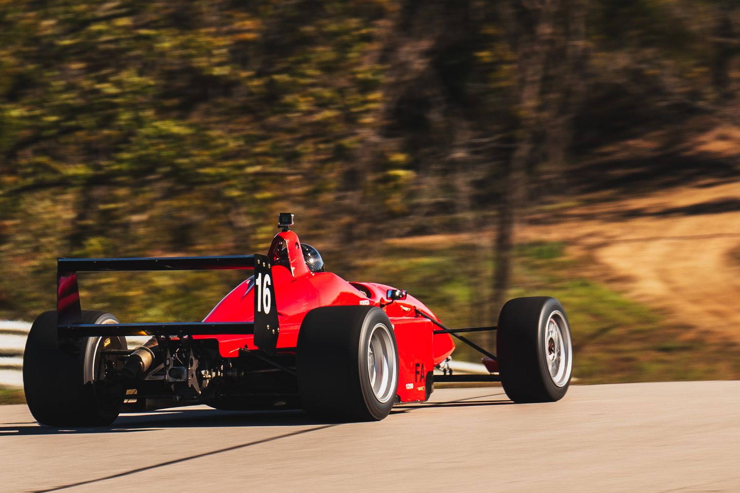 Red formula racing car speeding through a curved track on a sunny day.