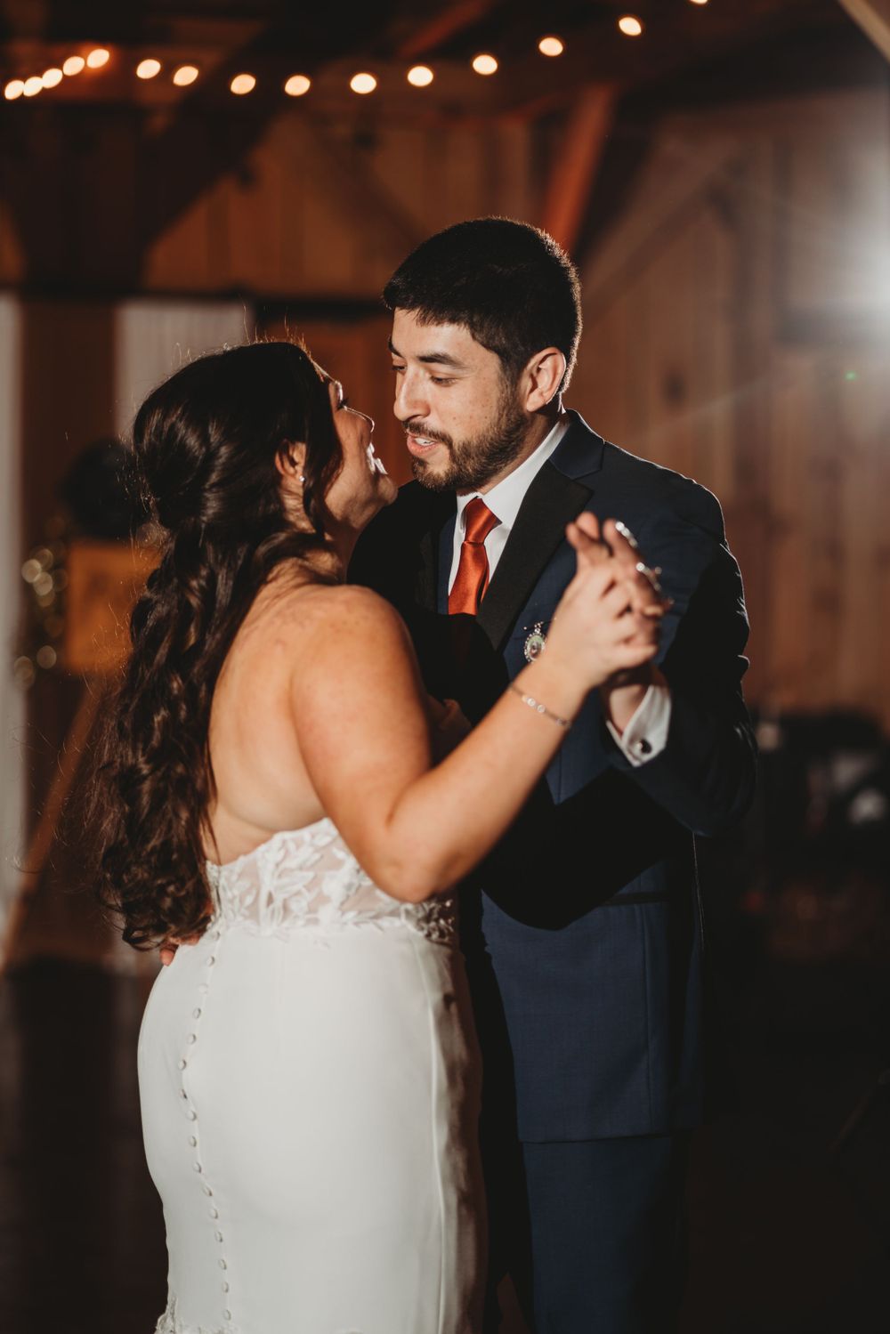 Couple shares their first dance in a warmly lit rustic barn venue.
