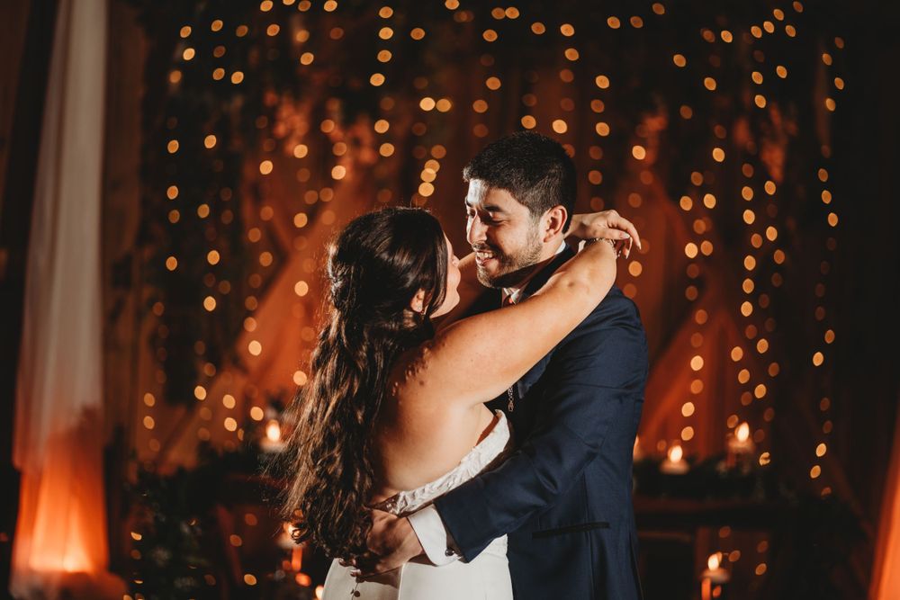 Romantic first dance moment captured with glowing string lights in background.