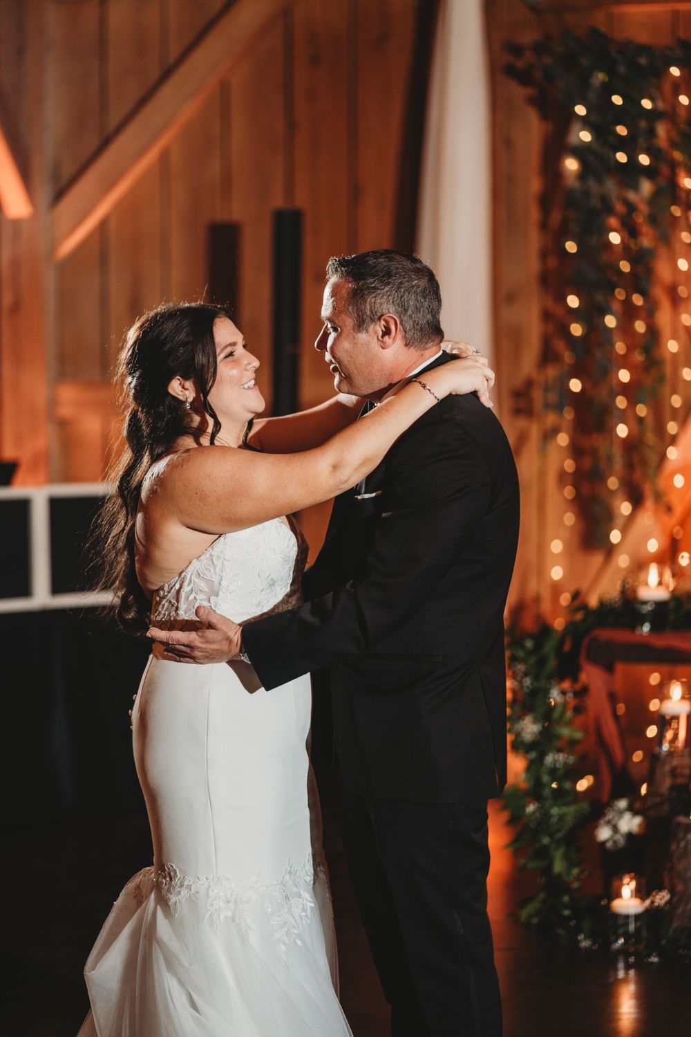 A romantic first dance moment between newlyweds in a warm barn venue with twinkling lights.