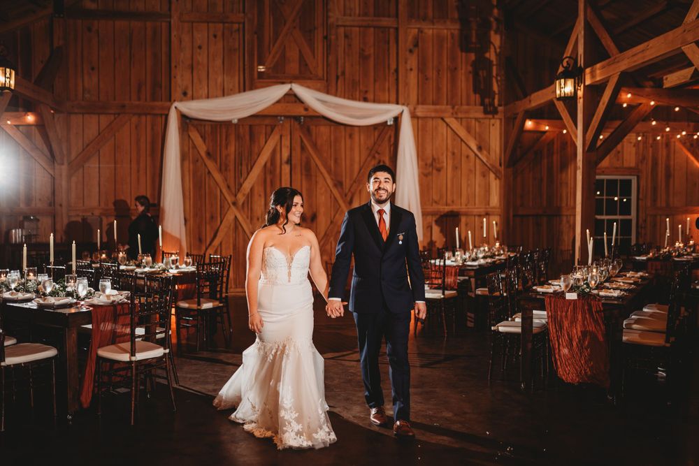 A couple poses in their wedding attire inside a beautifully decorated rustic barn venue.