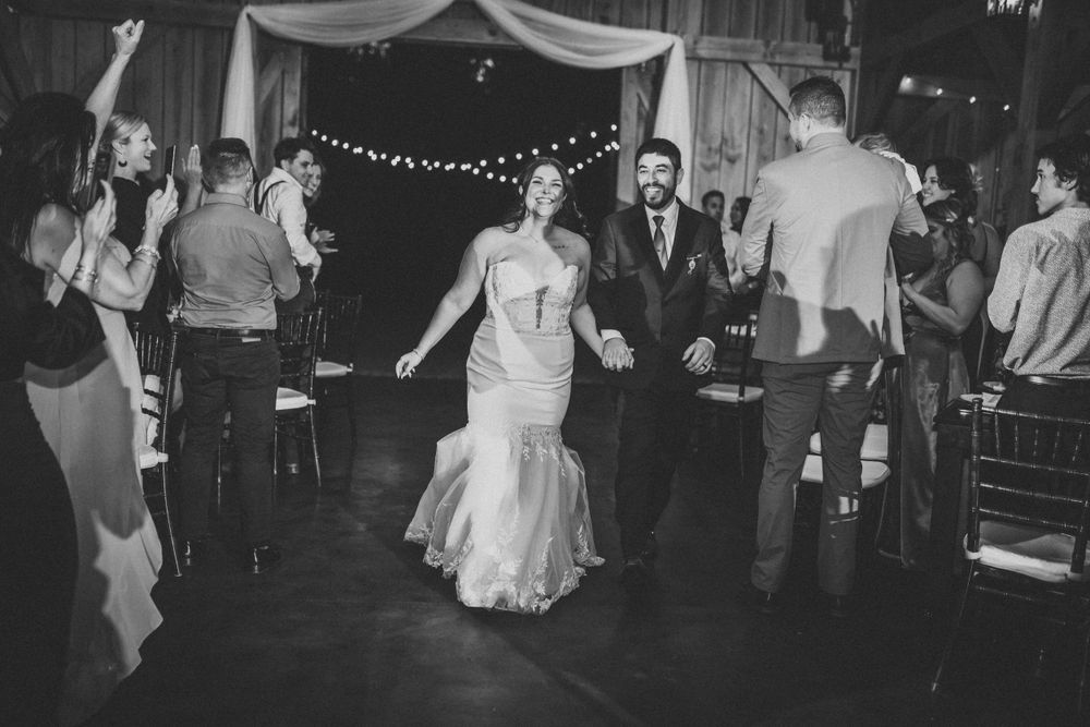 Wedding guests dancing and celebrating in a rustic barn venue with string lights.