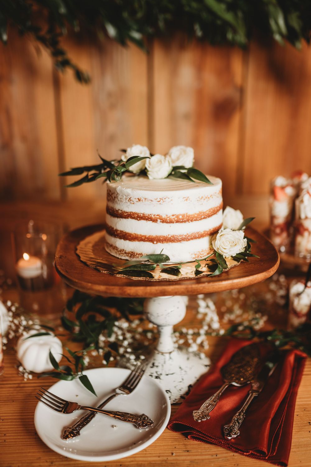 A rustic naked wedding cake decorated with white flowers on an elegant cake stand.
