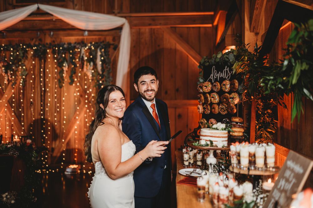 A rustic barn wedding dessert display with string lights and greenery.