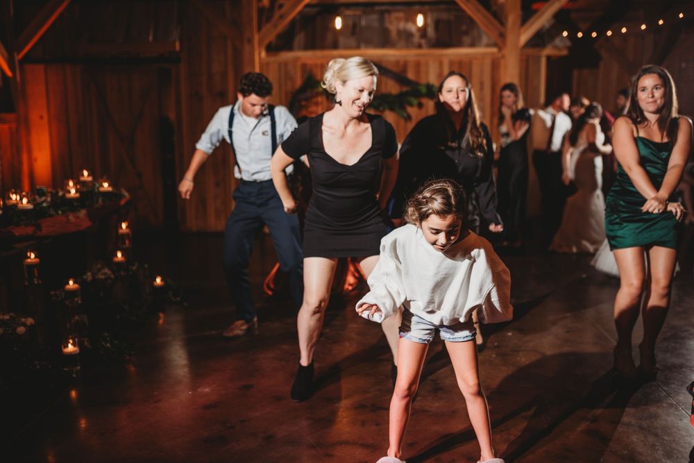 Guests dancing and having fun at a rustic barn wedding reception with string lights and dark ambiance.