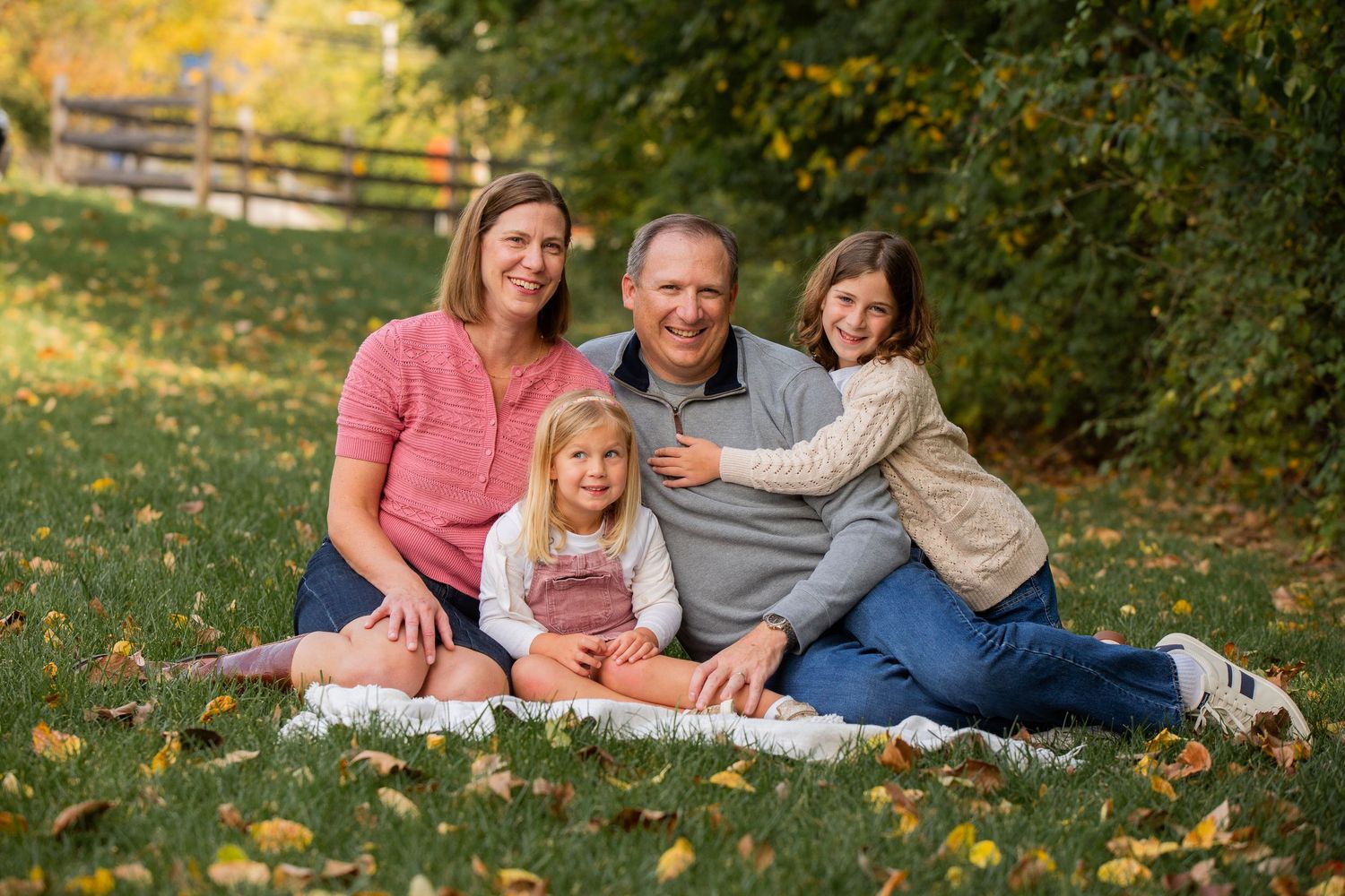 Family enjoying a casual outdoor photoshoot on a blanket in autumn grass and fallen leaves.