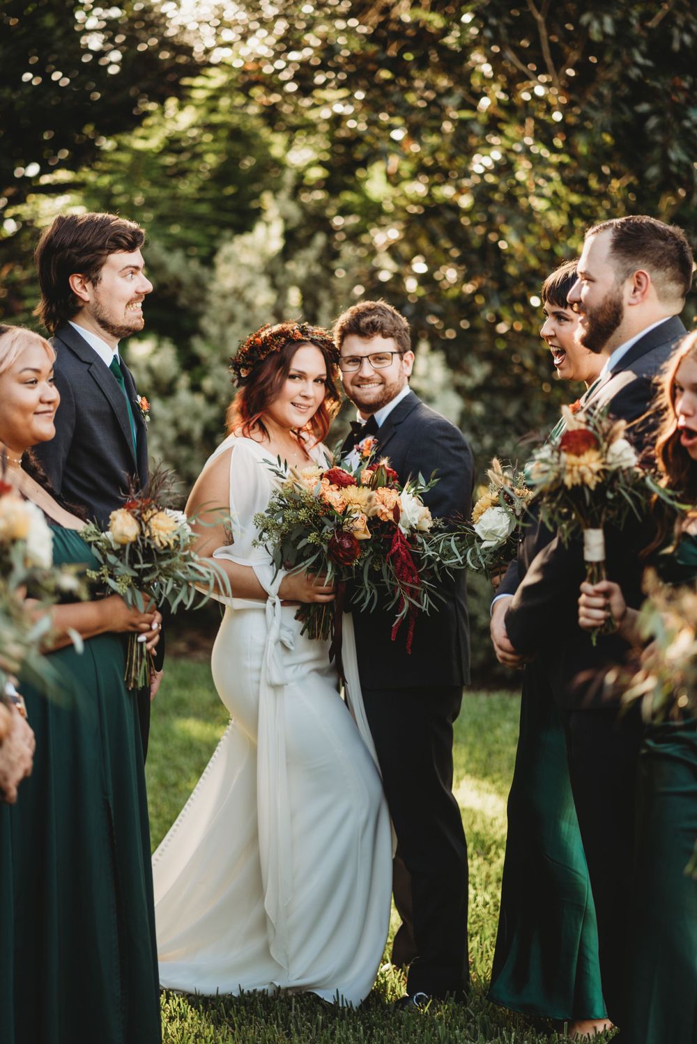 Wedding party gathering outdoors with emerald green dresses and autumn-themed bouquets.