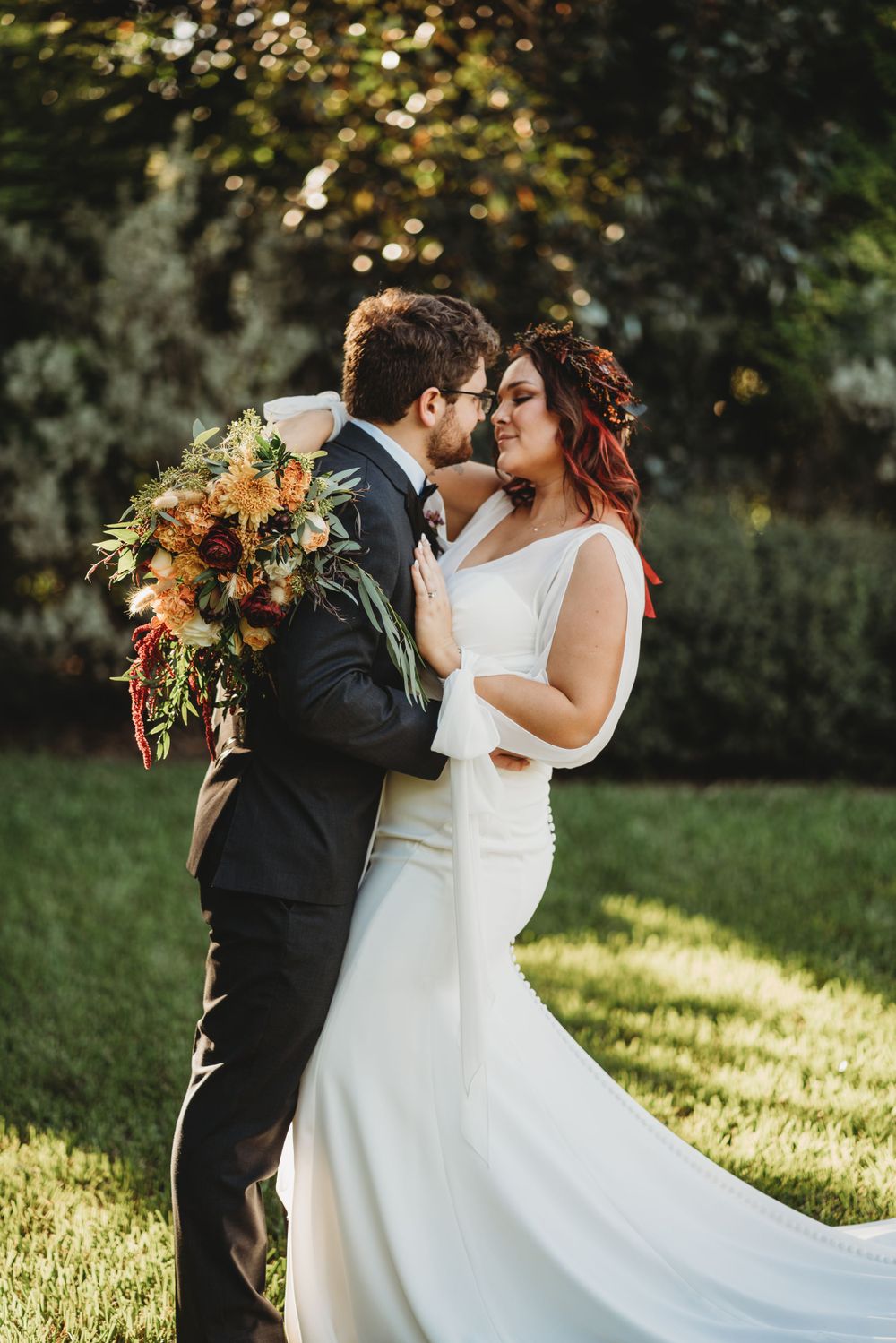 Romantic wedding couple embracing in golden sunset light with fall-colored bouquet.
