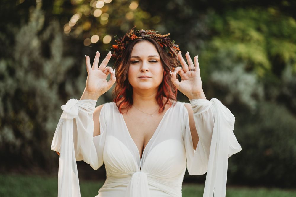 Bride in flowing white dress with dramatic sleeves poses playfully in garden setting.