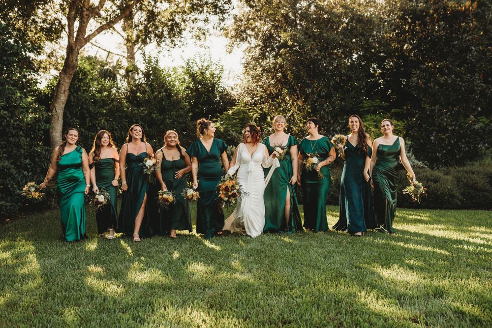 Bridal party in emerald green dresses posing together on sunny lawn.