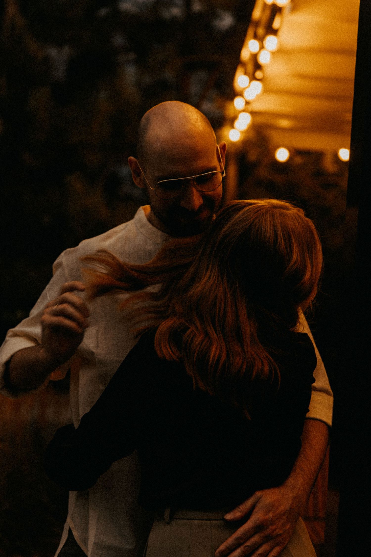 A couple shares an intimate dance moment under warm string lights.